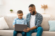 © Prostock-studio - African American Father Teaching Son To Use Laptop Browsing Internet At Home. Little Boy And His Dad Browsing Internet Or Watching Movie Online Together On Weekend. Modern Gadgets Lifestyle
