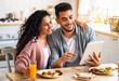 © Prostock-studio - Cheerful Middle Eastern Spouses Using Digital Tablet In Kitchen While Eating Breakfast, Happy Young Arab Couple Sitting At Table With Modern Gadget, Shopping Online Or Browsing Internet, Copy Space