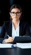 © srivilai - Professional Businesswoman in Black Suit at Desk With Clipboard and Paper in Office With Serious Expression Wearing Glasses
