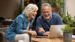 © Shahanaz - Joyful senior couple laughing together while using a laptop outdoors on a sunny day