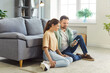 © Studio Romantic - Young couple sitting on floor of their cozy home using smart phone together, browsing social media, watching videos, planning trip, or shopping online. Electronic commerce, modern technology usage