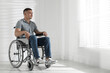 © New Africa - Young man in wheelchair near window indoors, space for text