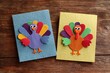 © Alena - Two colorful handmade Thanksgiving turkey cards made of textured paper, placed on a rustic wooden background, concept of festive crafts
