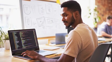 Focused developer programming at modern workspace with laptop and whiteboard