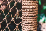Thick rope coils tightly around a cylindrical post beside a knotted net, both showcasing coarse, fibrous textures. Close-up emphasizes the rugged craftsmanship and maritime feel