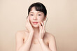 © kitthanes  - A beautiful young Asian woman with clean, fresh skin against a beige background. Skincare, facial treatment, cosmetology, beauty, and spa. An elegant portrait of an Asian woman.