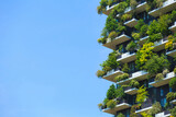 Vibrant vertical garden on energy efficient building, featuring lush greenery on balconies throughout the facade against a clear blue sky.