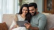 © Johannes - happy indian family couple using digital tablet computer at home smiling young husband and wife watching tv video calling or doing online ecommerce shopping together sitting on couch in living room n