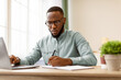 © Prostock-studio - Black Businessman Taking Notes Sitting At Laptop Writing In Notebook Working At Workplace In Modern Office. Entrepreneurship And Business Career Concept, Selective Focus
