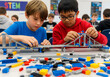 © homydesign - Two boys, one wearing glasses, build a bridge with colorful blocks, focusing intently on their creation in a classroom environment