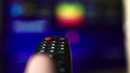 Man controls TV with modern remote control. Watch Smart TV and use remote control. Male hand selecting internet TV channels with remote control, close-up. Scrolling through blurred TV pages