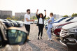 © sofiko14 - A woman celebrates her new car purchase at a dealership with a salesperson and her partner nearby. Cars of various models are in the background.