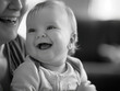 © Delara - A monochrome image featuring a joyful baby being held by a smiling adult in soft focus view
