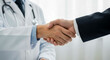 © Norah Allen - A medical professional in a white lab coat and stethoscope shakes hands with a person in a dark suit doctor healthcare handshake business agreement partnership