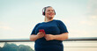 © RZ Images - Outdoor Portrait of Body Positive Overweight Woman Using Red Smartphone Phone Outdoors at City in the Morning. Wearing Red Headphones
