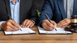 © PaulShlykov - Businessmen signing documents during a formal meeting in an office setting