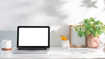 Wall Mural - Laptop with blank white screen on desk, surrounded by a coffee mug, green plant, and office supplies.