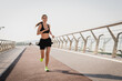 © InsideCreativeHouse - Female runner in activewear burning calories with a cardio workout. Sporty woman jogging running on city park bridge outdoors. Woman exercising with earphones on in the morning. Copy space