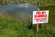 © Ulrich - Sign warning for blue-green algae by a contaminated pond with water lilies, advising to avoid contact with water