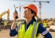 © tebu - A construction worker wearing an orange hard hat and vest holds a walkietalkie at a construction site