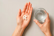 © Nargiz - High resolution, ultra realistic photo of a woman’s hands holding three white capsules and a clear glass of water on a beige background. Clean, minimalistic layout ideal for supplement, vitamin ads