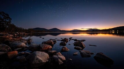 Wall Mural - a picture featuring a body of water with rocks in the foreground and a distant mountain range under 