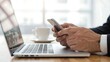 © FARVEZ - Businessman using smartphone and laptop with coffee nearby