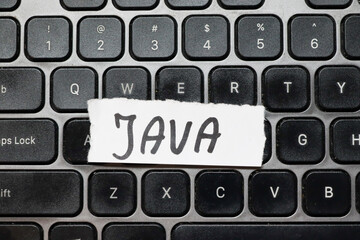 handwritten note reading java placed on a black computer keyboard. java is a popular programming lan