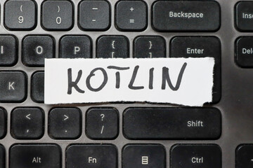handwritten word kotlin on a white paper strip placed on a black keyboard, symbolizing programming l