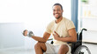 © Prostock-studio - Physical rehabilitation for with disability people. Happy black guy in wheelchair making exercises with dumbbell at home. Cheerful young man working out with weights indoors