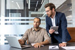 © Liubomir - Two business professionals collaborating in an office setting, discussing data on a laptop and tablet.