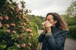 © Ryan - Woman with allergies sneezing near blooming flowers outdoors