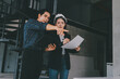 © ARMMY PICCA - Construction manager and engineer dressed in orange work vests and hard helmets explore construction documentation on the building site near the steel frames