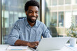 © Maria Vitkovska - Smiling black businessman working on laptop in modern office
