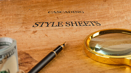 a wooden surface holds a pen and a magnifying glass alongside a rolled-up currency note, emphasizing