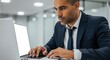 © Creative Hero - Man in dark suit and tie intently typing on a laptop with blank screen office computer