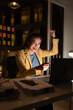 © SOMKID - Excited young Asian woman with laptop at work desk in office a night time, feeling joy celebrating  woman.