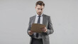 © Oleksandr - Young businessman in grey suit holding clipboard. Ready to write information with pen. Attractive, presentable professional man with confident expression. Corporate worker stands with paper in hand.