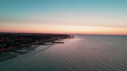 Wall Mural - Aerial sunset over coastal town with tranquil waves and pastel skies