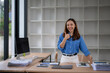 © Wasana - A woman is standing in front of a desk with a laptop and papers