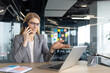 © Liubomir - A businesswoman in a modern office uses a laptop and talks on the phone, gesturing with her hand while smiling.