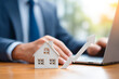 © MOSTFAOZIA - Businessman's hand using a laptop and standing next to a house model with a growth arrow icon on the table