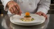 © ZaheerUDin - Chef garnishing a scallop dish with an orange flower and herbs on a white plate in a kitchen setting