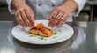 © ZaheerUDin - Chef plating a salmon fillet with edible flower and herbs on a white plate in a professional kitchen