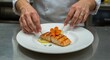 © ZaheerUDin - Chef preparing grilled salmon with edible flower and lemon on a white plate in a restaurant kitchen