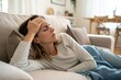© Ployker - Young woman with headache resting on sofa with hand on forehead - stress relief and wellness at home