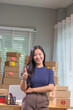 © NANKHAMMAI - A young Asian entrepreneur smiles as she types on her laptop, managing inventory, packing packages and checking orders for her online startup business.