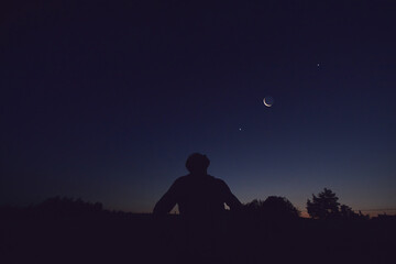 Wall Mural - silhouette of a man observing moon, milky way stars, planets and other celestial objects from a dark