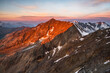 © PATMALUPHOTO - A high-angle view of rugged, rocky mountains, some snow-capped, under a pink and orange sky at sunset. Mantova refuge al Vioz, Peio, Trentino. The sun casts a shadow across the center peak.