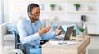 © Prostock-studio - Black guy with disability with headset communicating online on laptop, having business meeting from home. Millennial African American man in wheelchair working in call center remotely